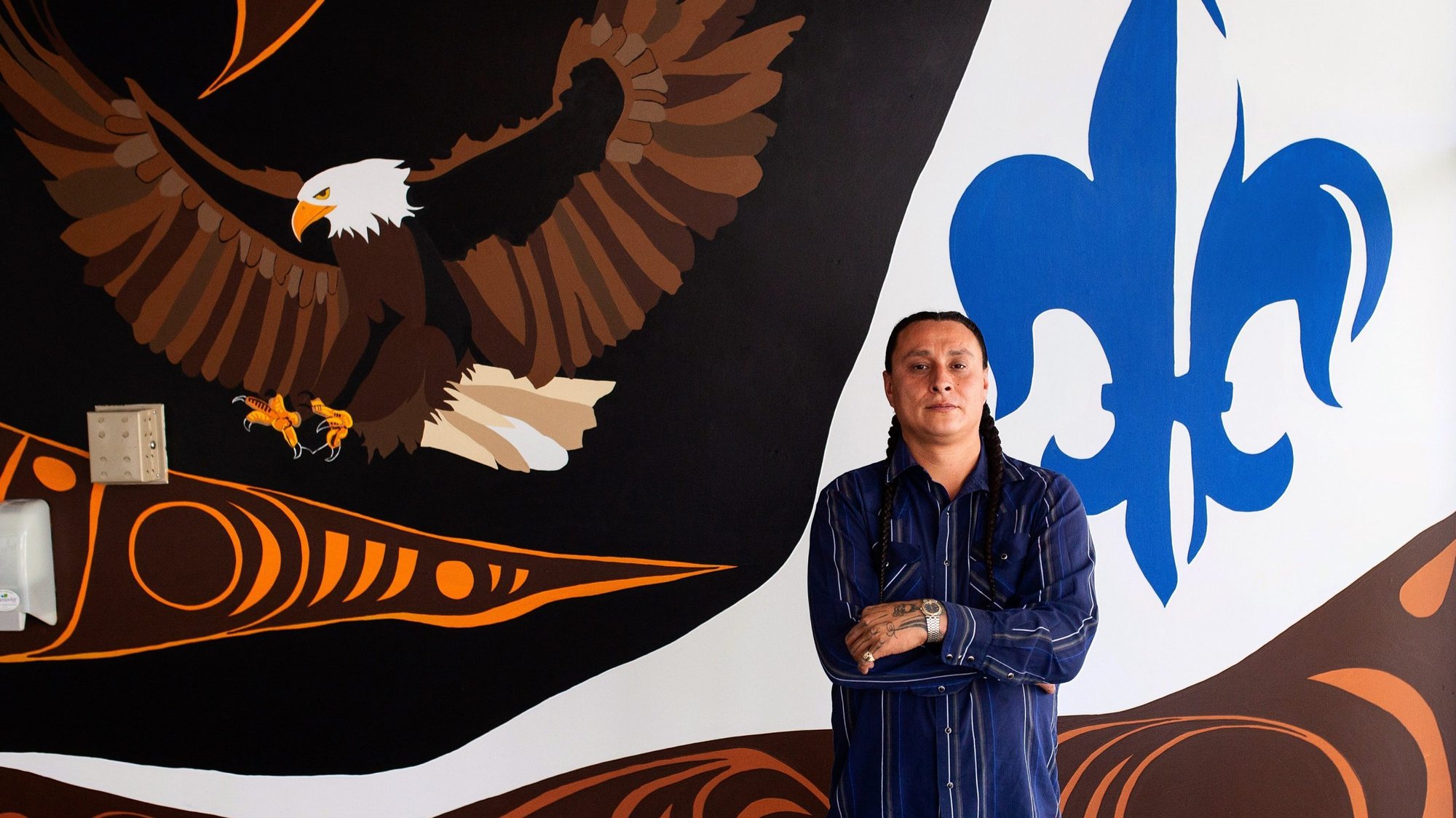 Indigenous artist Ryan Willert poses Aug. 28, 2020, before the mural he painted at Ecole Camille J. Lerouge School in Red Deer, Alberta. The 36-year-old Blackfoot from the Siksika Nation is well-known in Alberta. (CNS photo/courtesy Kyiah Kristina via Catholic Register)