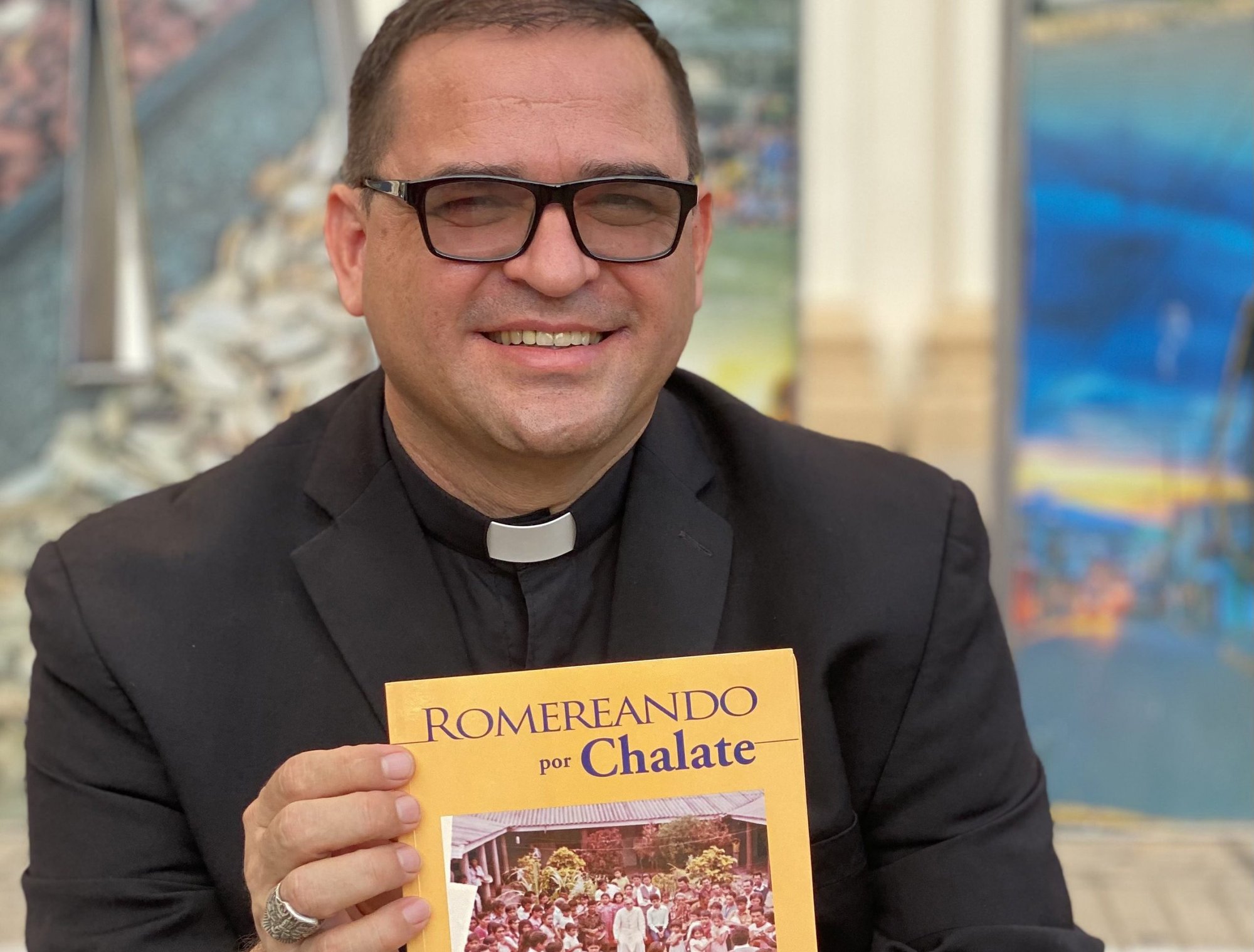 Bishop Oswaldo Escobar of Chalatenango, El Salvador, poses March 17, 2021, in front of the diocesan cathedral with his recently published book about St. Oscar Romero. The book narrates the soft side of St. Romero in the agricultural diocese in northern El Salvador. (CNS photo/courtesy Diocese of Chalatenango)