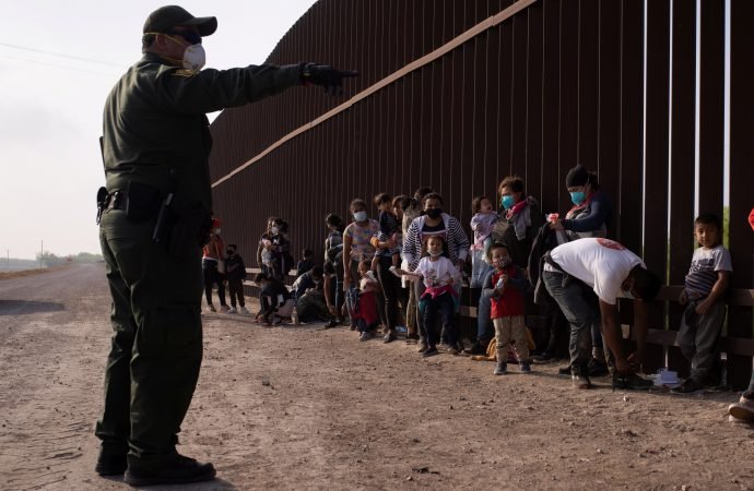 A Border Patrol agent in Penitas, Texas, instructs asylum-seeking migrants March 17, 2021, as they line up along the border wall after crossing the Rio Grande. Immigration and Customs Enforcement reports more than 12,000 coronavirus cases in detention centers. (Adrees Latif/Reuters via CNS)