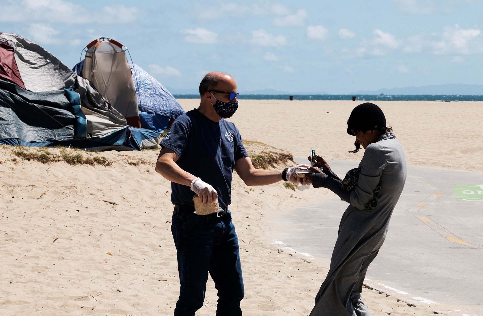 The Order of Malta’s Mike Psomas offers food and a hygiene kit to a resident of the growing homeless encampment along the Venice Beach boardwalk. (Victor Alemán)