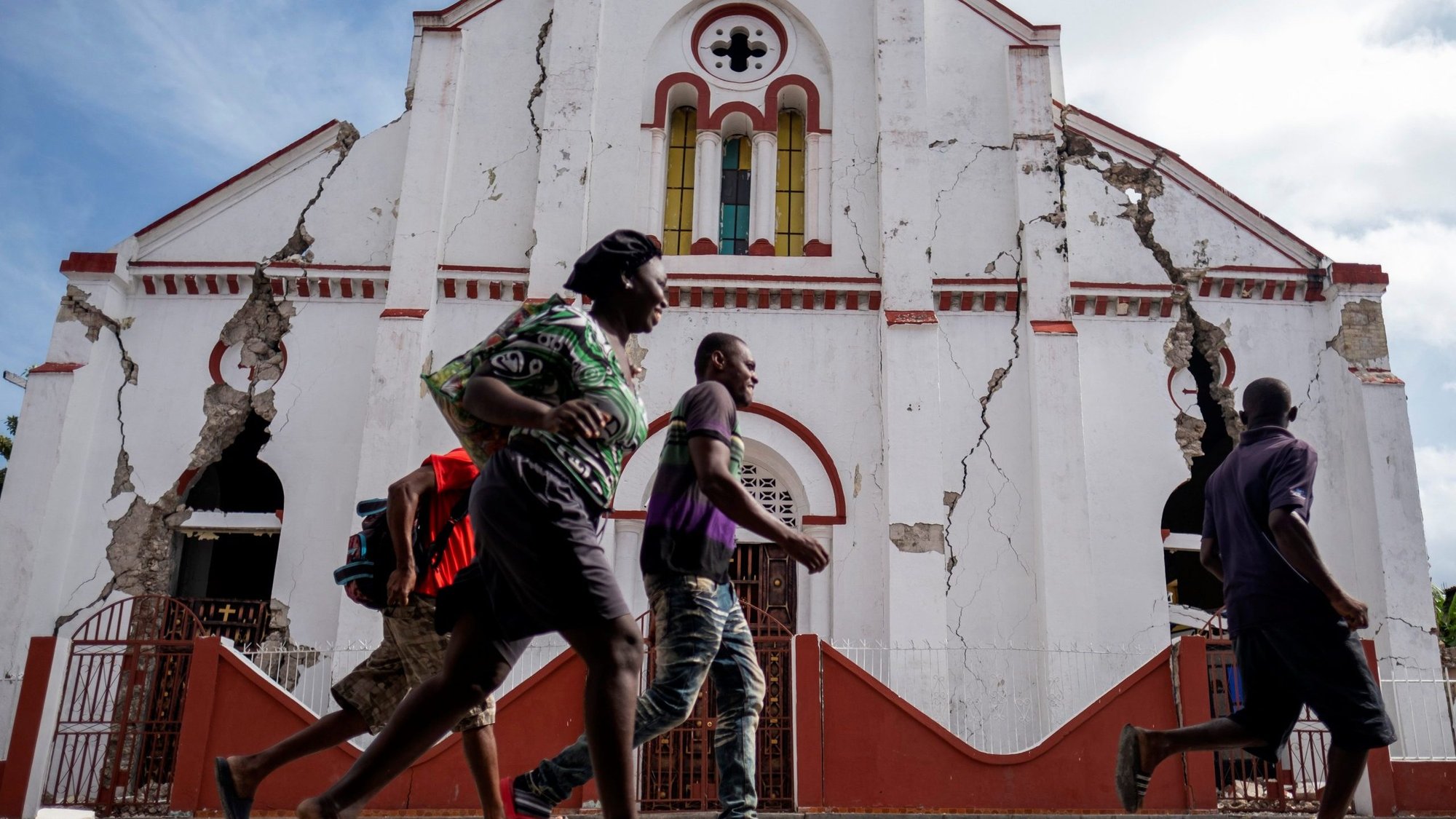People run past in front of a heavily damaged church in Les Cayes, Haiti, Aug. 18, 2021, after a 7.2 magnitude earthquake rocked the area four days earlier. (CNS photo/Ricardo Arduengo, Reuters)