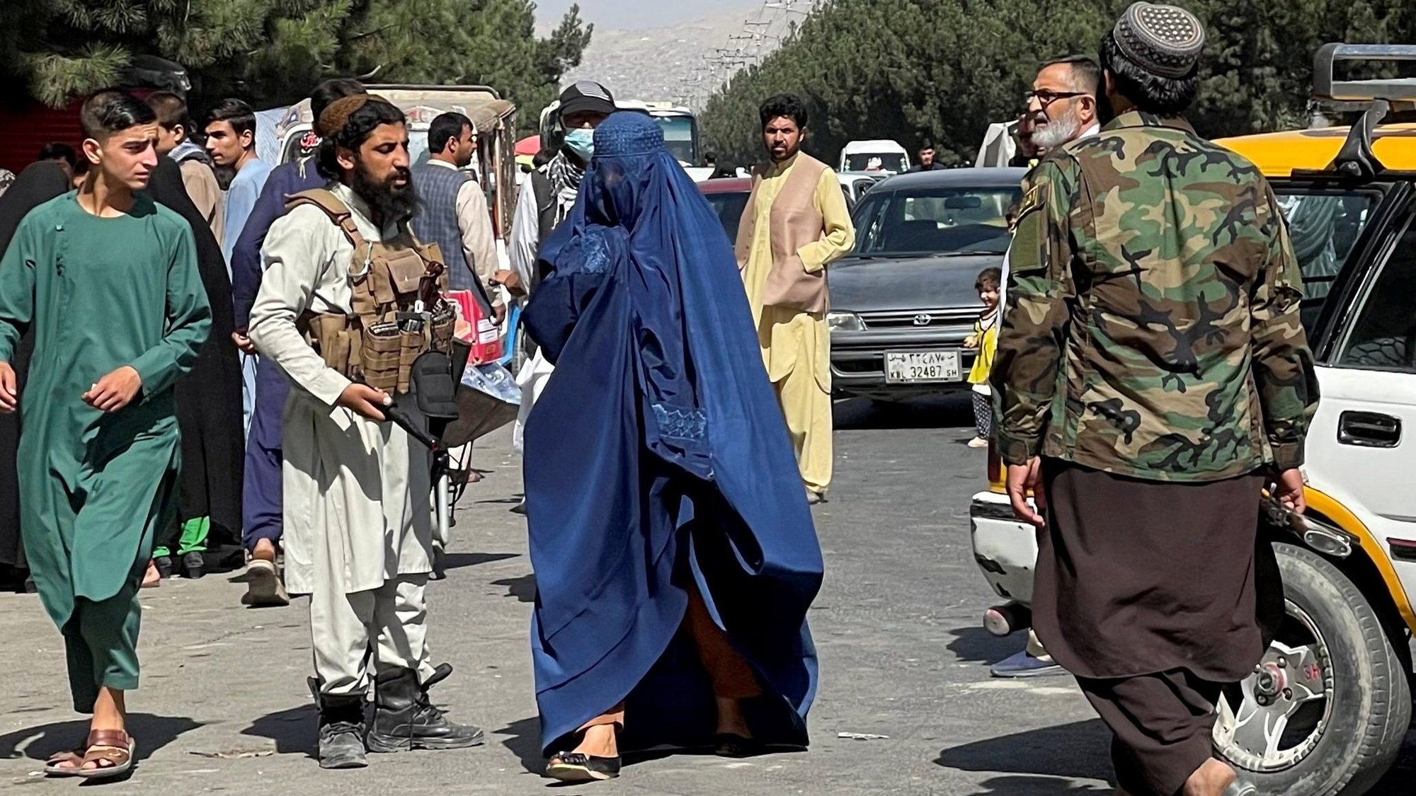 A member of the Taliban forces talks block the roads around Kabul airport as a woman wearing a burqa walks past Aug. 27, 2021. Religious minorities and women are concerned about their treatment at the hands of the Taliban and other religious extremists. (CNS photo/Stringer, Reuters) NO ARCHIVES. MUST DISCARD 30 DAYS AFTER DOWNLOAD.