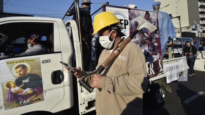 A worker walks past a truck carrying a poster of San Cayetano. People observing the feast day of the patron saint of labor marched to Plaza de Mayo to demand work and better wages, Buenos Aires, Saturday, May 7, 2021. (Gustavo Garello/AP via Crux)
