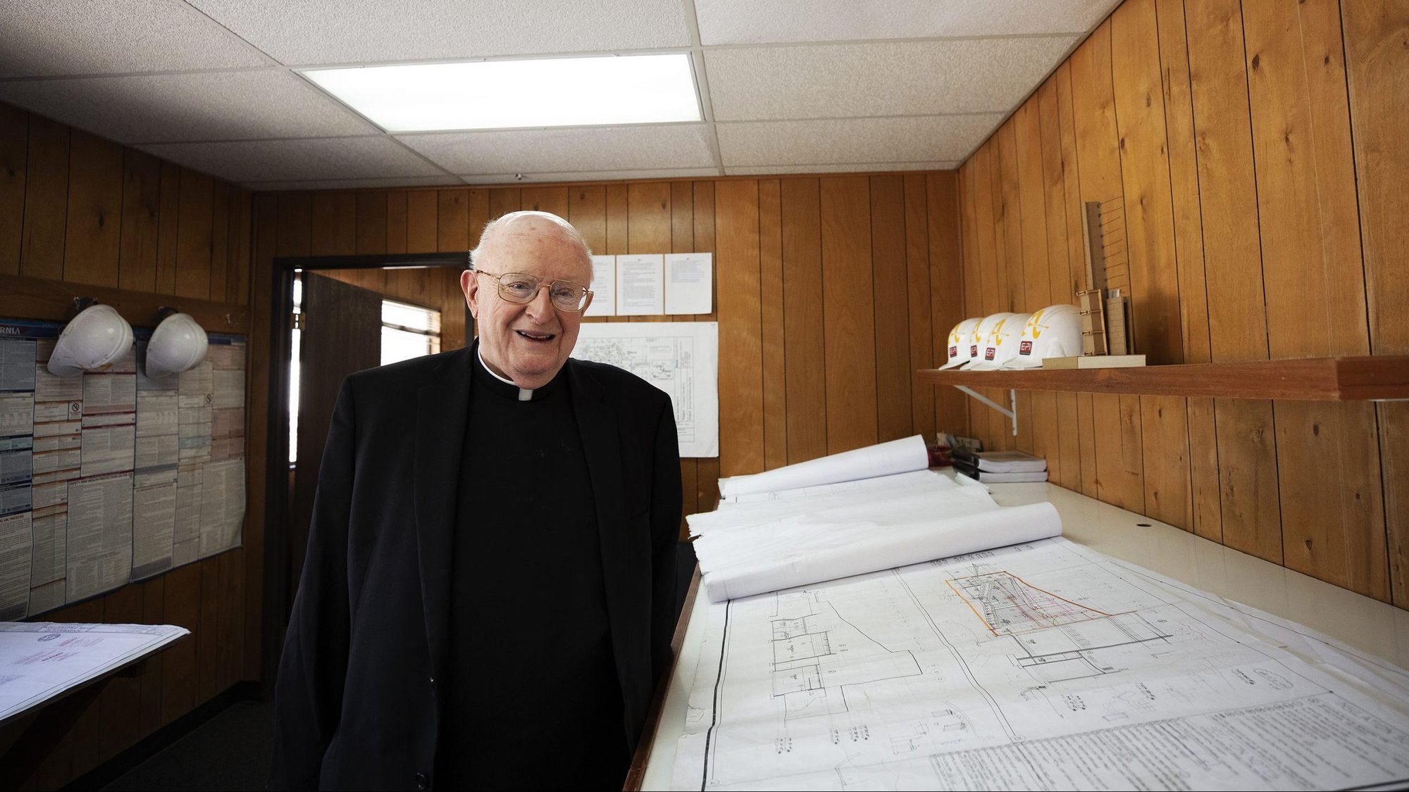 Msgr. Aidan Carroll stands next to blueprints for the new performing arts center at Bishop Amat High School, a project he has spearheaded for more than a decade. The building is set to open this fall. (Victor Alemán)