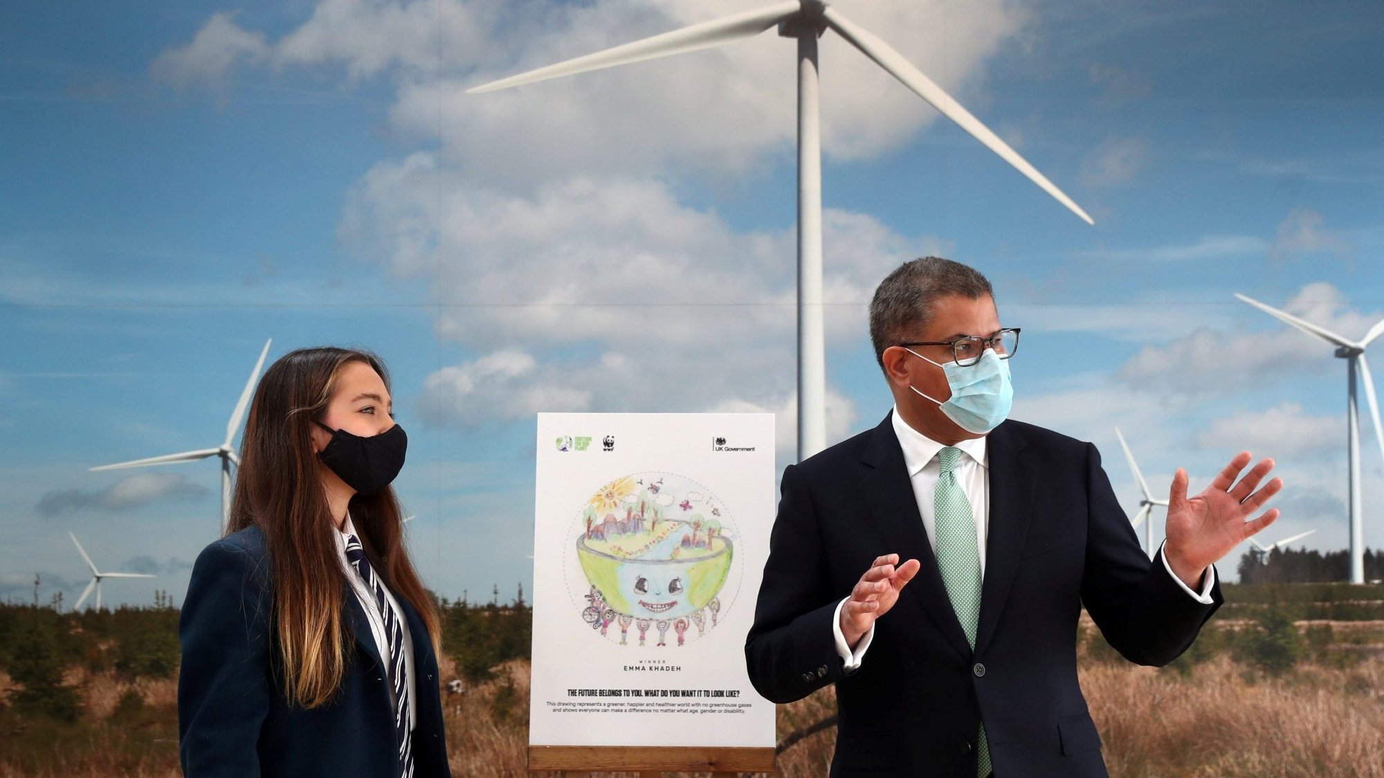 Alok Sharma, president of the U.N. Climate Change Conference, gestures next to Emma Khadeh and her winning art competition piece, during an event at Whitelee Windfarm, marking six months until the U.N. Climate Change Conference, outside Glasgow, Scotland, May 14, 2021. In a late August radio interview, Pope Francis confirmed that he will attend U.N. Climate Change Conference in Glasgow in November this year. (CNS photo/Russell Cheyne, Reuters pool)