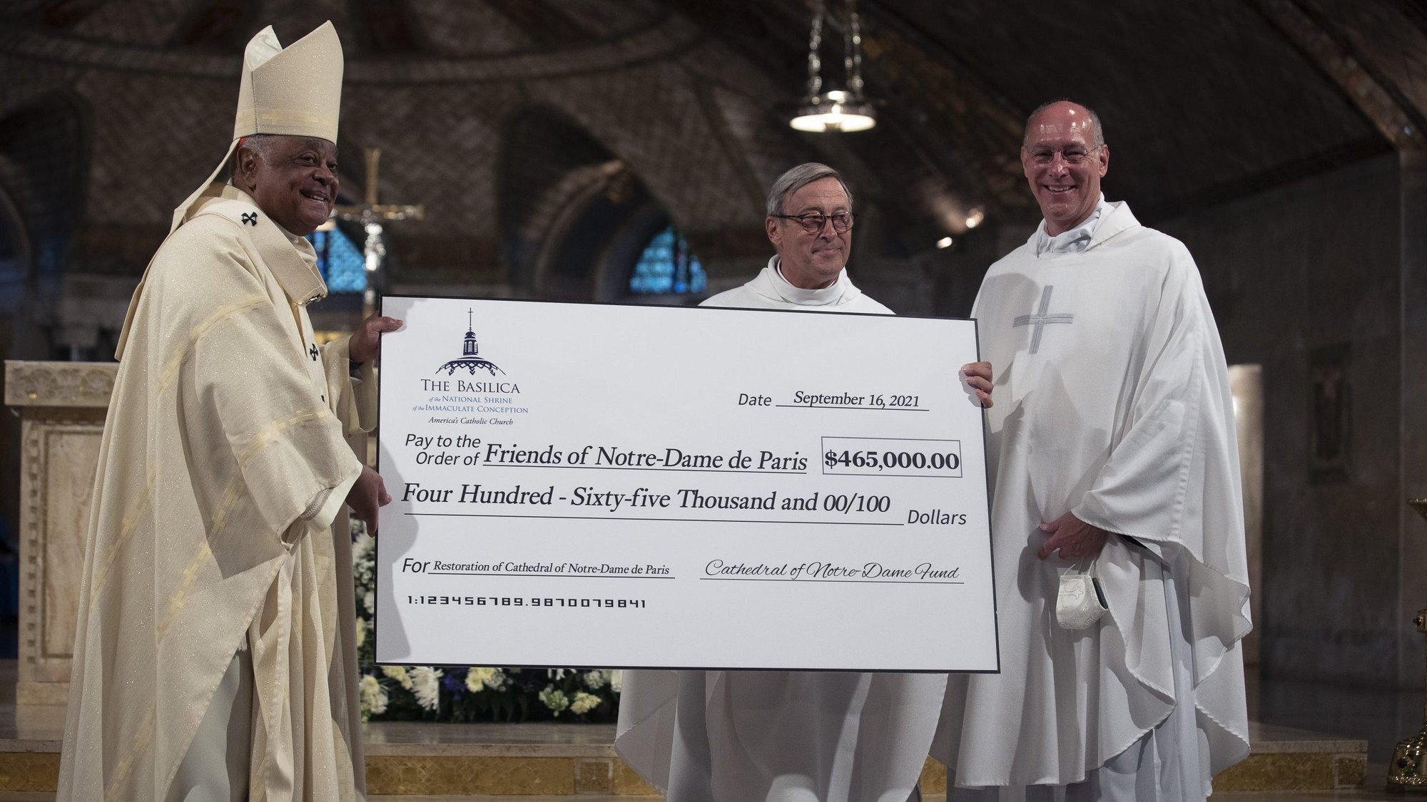 Msgr. Patrick Chauvet, center, rector of the Notre Dame Cathedral in Paris, receives a check from Msgr. Walter Rossi, rector of the Basilica of the National Shrine of the Immaculate Conception in Washington, and Washington Cardinal Wilton D. Gregory after a special Mass in in the basilica's Crypt Church in Washington Sept. 16, 2021. The funds are for restoration efforts of the historic cathedral in France. (CNS photo/Tyler Orsburn)
