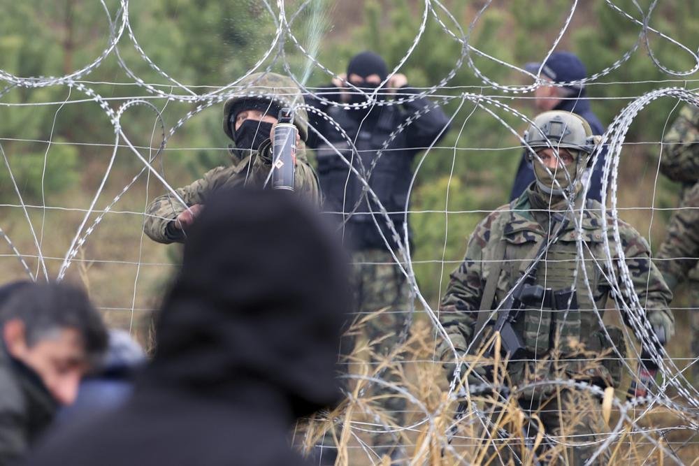 Polish border guards stand near the barbed wire as migrants from the Middle East and elsewhere gather at the Belarus-Poland border near Grodno, Belarus, Monday, Nov. 8, 2021. Poland increased security at its border with Belarus, on the European Union's eastern border, after a large group of migrants in Belarus appeared to be congregating at a crossing point, officials said Monday. The development appeared to signal an escalation of a crisis that has being going on for months in which the autocratic regime of Belarus has encouraged migrants from the Middle East and elsewhere to illegally enter the European Union, at first through Lithuania and Latvia and now primarily through Poland. (Leonid Shcheglov/BelTA via AP/Crux)