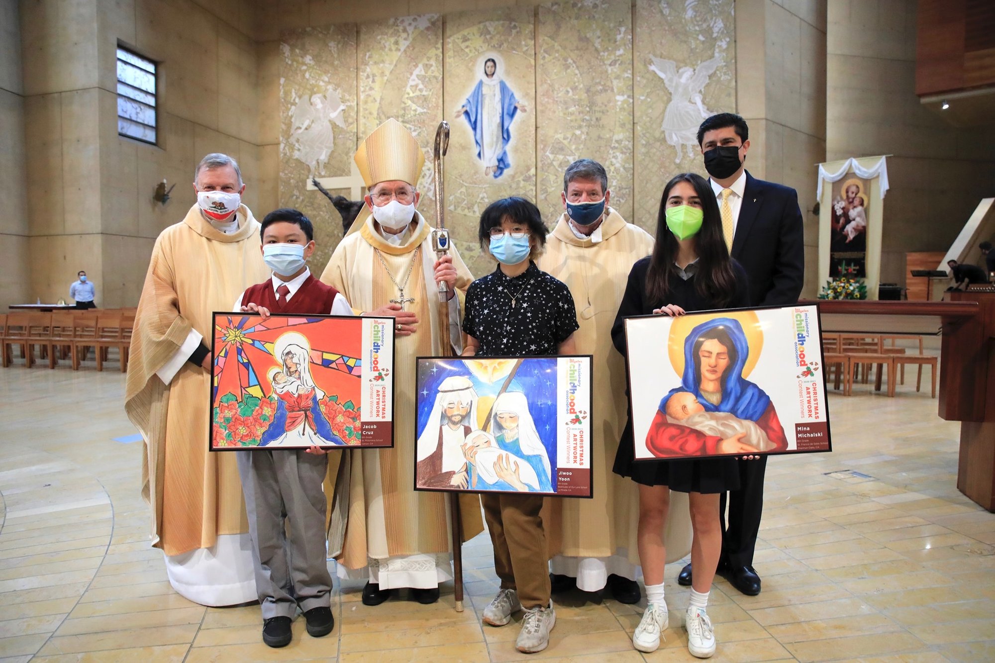 From left: Jacob Cruz, Justina Yoon, and Mina Michalski pose with their award-winning artwork at the Missionary Childhood Association Mass Oct. 20, 2021, at the Cathedral of Our Lady of the Angels. Behind them, from left to right are: Msgr. Kieran E. Harrington, national director of the Pontifical Mission Societies in the U.S.; Archbishop José H. Gomez, and Msgr. Terrance Fleming, Pontifical Mission Societies executive director for the Archdiocese of Los Angeles, and Catholic Schools superintendent Paul Escala. (David Amador Rivera)
