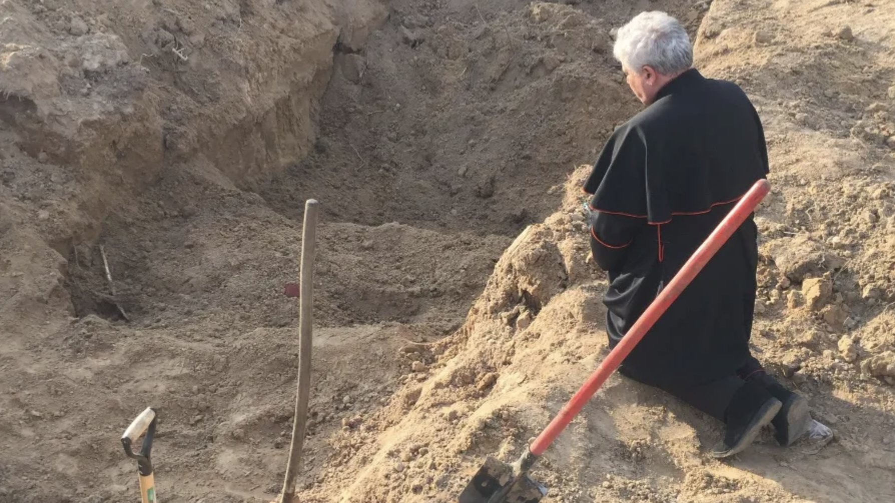 Papal envoy Cardinal Konrad Krajewski prays at a mass grave in Ukraine on Good Friday, April 15, 2022. (Vatican Media via CNA)