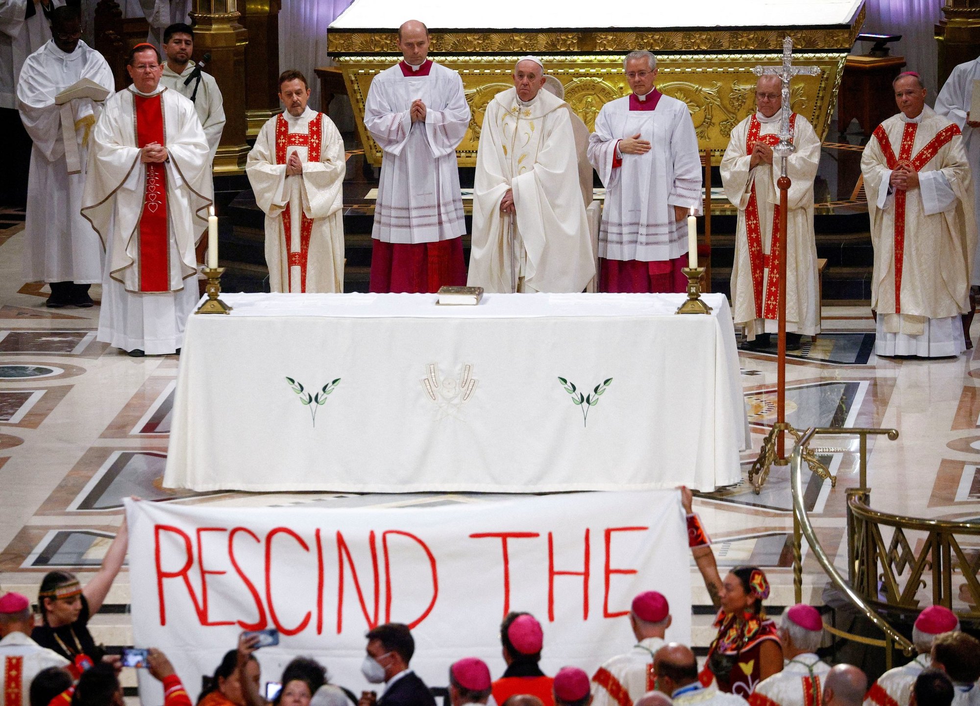 Indigenous people hold a banner calling on Pope Francis to "rescind the doctrine," an apparent reference to the so-called doctrine of discovery, a collection of old papal teachings that encouraged explorers to colonize and claim the lands of any people who were not Christian, placing both the land and the people under the sovereignty of European Christian rulers. The incident occurred during a papal Mass at the National Shrine of Sainte-Anne-de-Beaupré in Quebec July 28, 2022. (CNS photo/Guglielmo Mangiapane, Reuters)