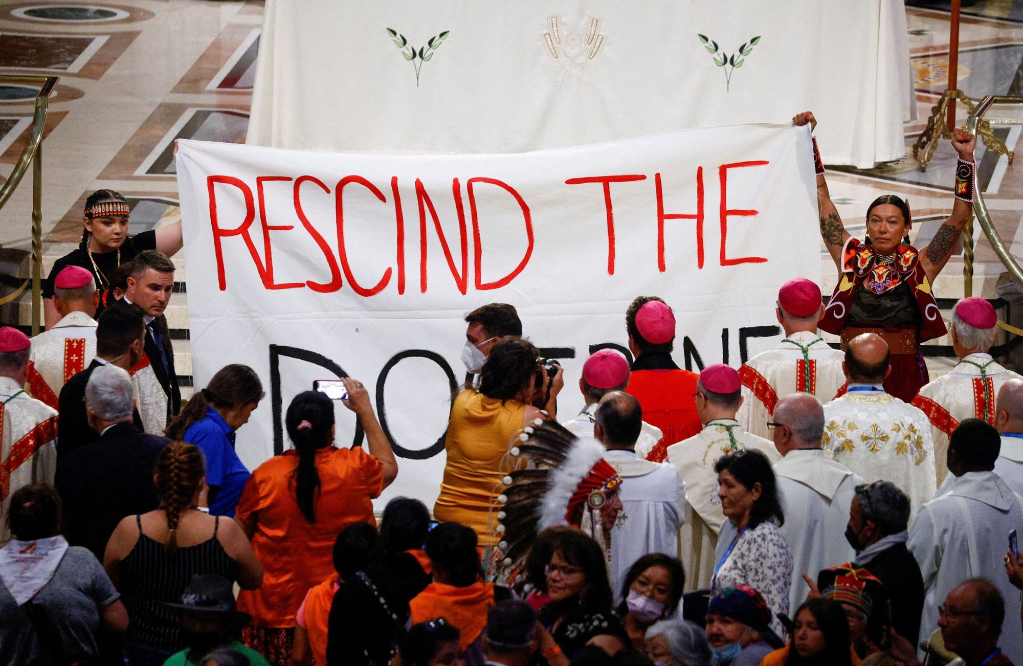 Indigenous people hold a banner calling on Pope Francis to "rescind the doctrine," an apparent reference to the so-called Doctrine of Discovery, a collection of old papal teachings that encouraged explorers to colonize and claim the lands of any people who were not Christian, placing both the land and the people under the sovereignty of European Christian rulers. The incident occurred during a papal Mass at the National Shrine of Sainte-Anne-de-Beaupré in Quebec July 28, 2022. (CNS photo/Guglielmo Mangiapane, Reuters)