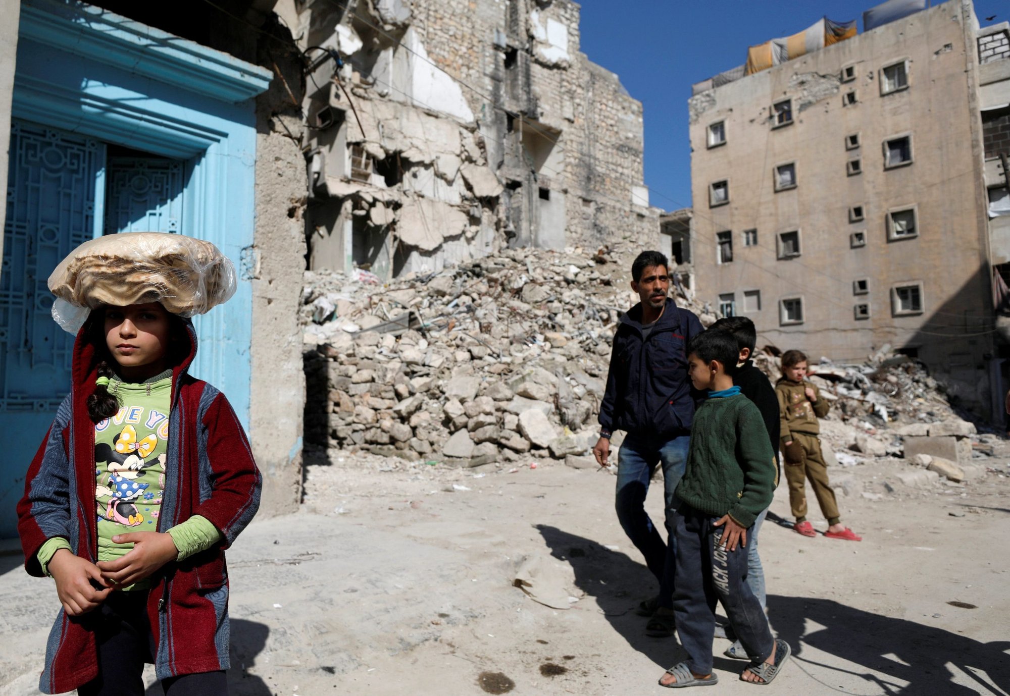 A girl carries a stack of pita bread on her head as she walks near rubble of damaged buildings in Aleppo, Syria, April 12, 2019. The Chaldean Catholic bishop of Aleppo said 11 years of war and the accompanying economic sanctions have left the city impoverished. (CNS photo/Omar Sanadiki, Reuters)
