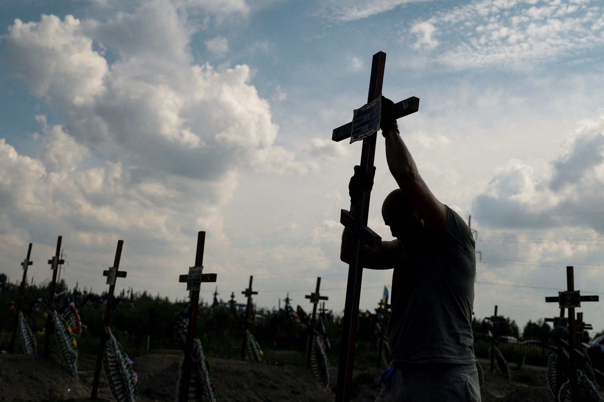 A volunteer places a cross with a number on a grave of an unidentified person during a mass burial ceremony in Bucha, Ukraine, Aug. 17, 2022, as Russia's attack on Ukraine continues. (CNS photo/Valentyn Ogirenko, Reuters)