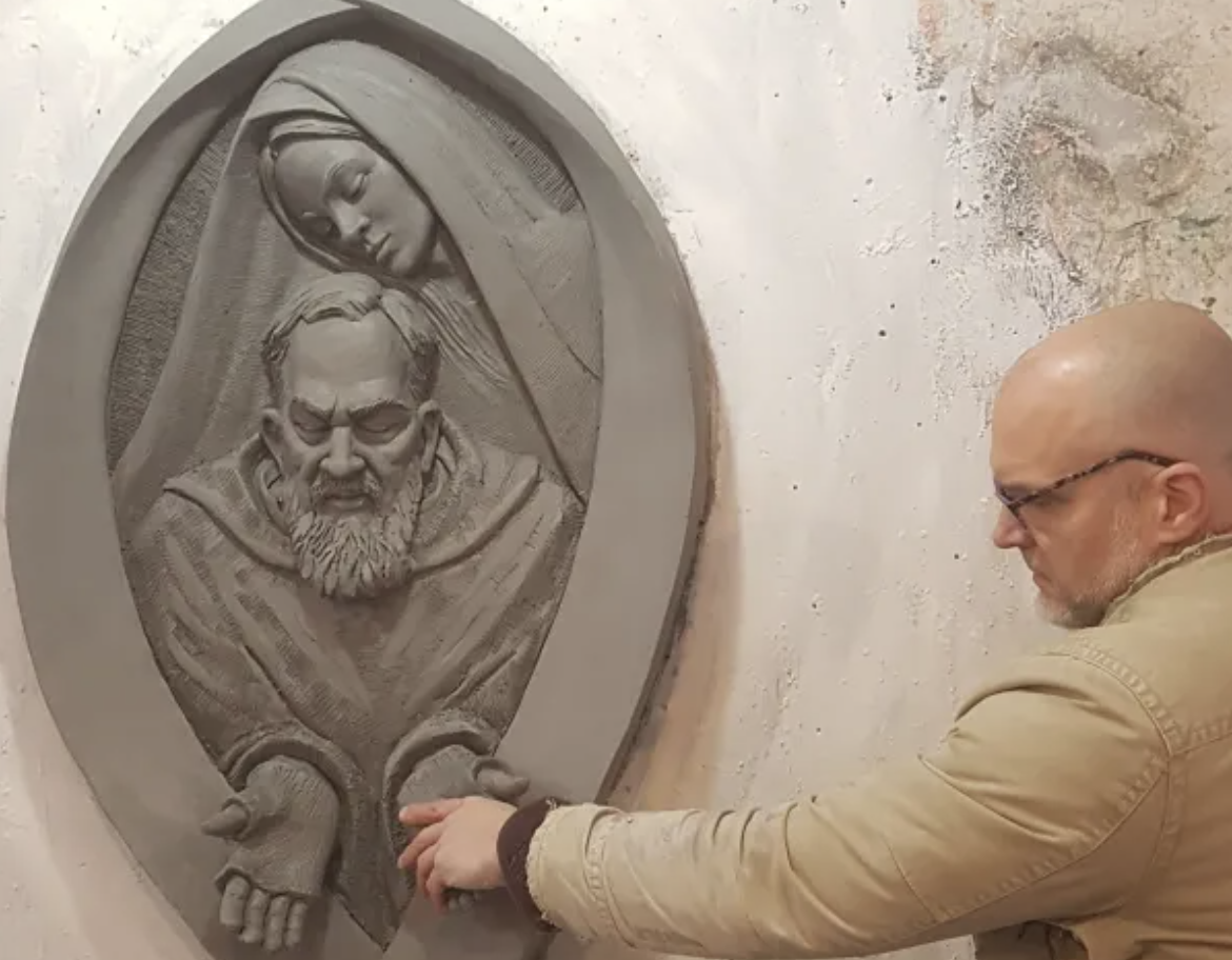 Artist Timothy P. Schmalz touches the hands of Padre Pio in his sculpture that includes the Blessed Virgin Mary. (Courtesy of Timothy P. Schmalz via CNA)