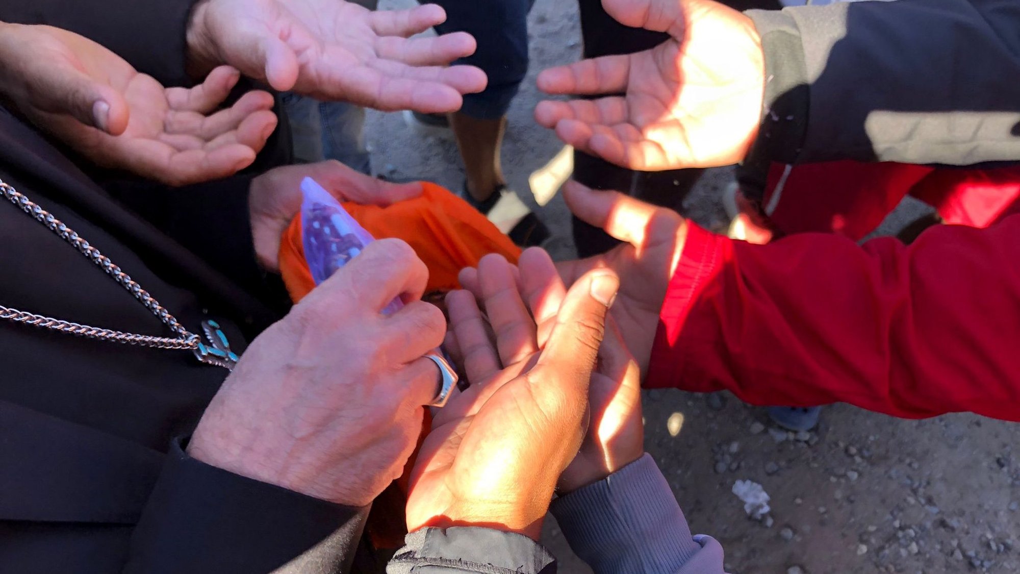 Venezuelan migrants squeeze in to grab a rosary from the hands of Bishop Mark J. Seitz of El Paso, Texas, during his visit to a tent camp on the banks of the Rio Grande on the Mexico side close to El Paso Oct. 29, 2022. The bishop has spoken out against the measure known as Title 42, which keeps certain migrants out of the U.S. citing health measures deemed necessary during the coronavirus pandemic. (CNS photo/courtesy Hope Border Institute)