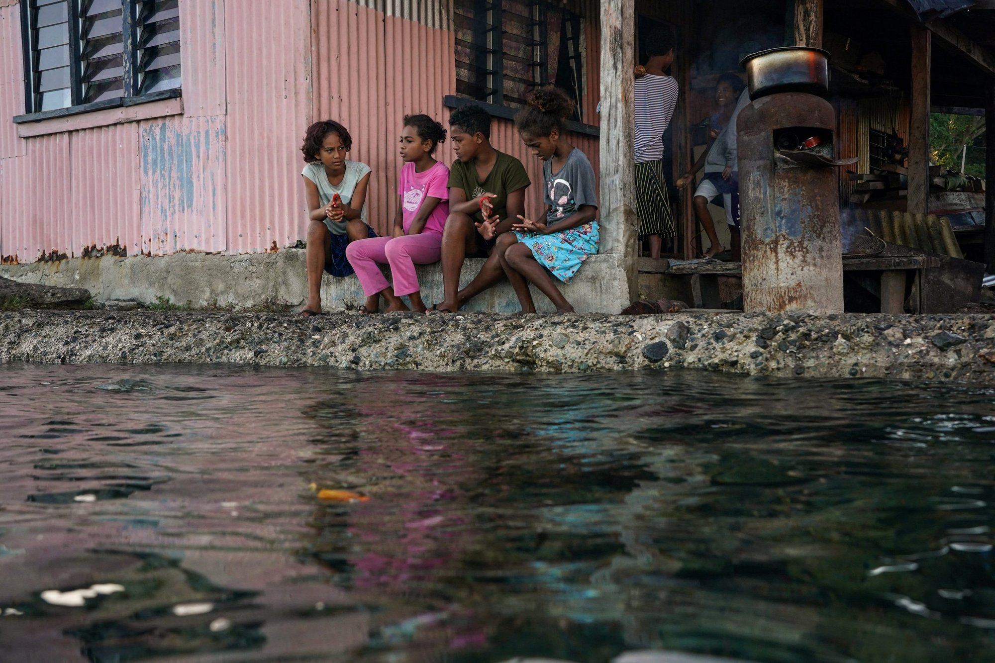 Village children pass the time in front of a home next to a flooding sea wall at high tide in Serua Village, Fiji, July 15, 2022. As the community runs out of ways to adapt to the rising Pacific Ocean, the 80 villagers face the painful decision whether to move. (CNS photo/Loren Elliott, Reuters)