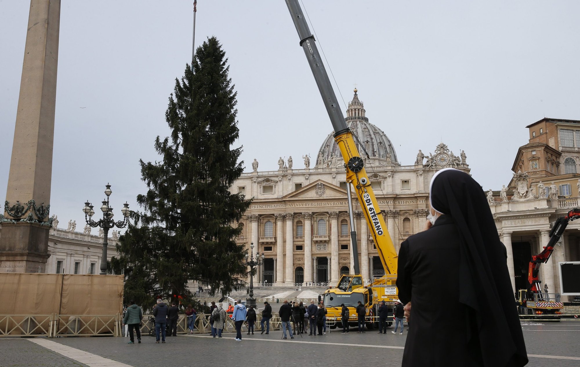 A nun watches as the Christmas tree is positioned in St. Peter's Square at the Vatican Nov. 23, 2021. After a controversy over the selection of this year's Vatican Christmas tree, the Vatican will receive a tree from an Italian tree farm. (CNS photo/Paul Haring)