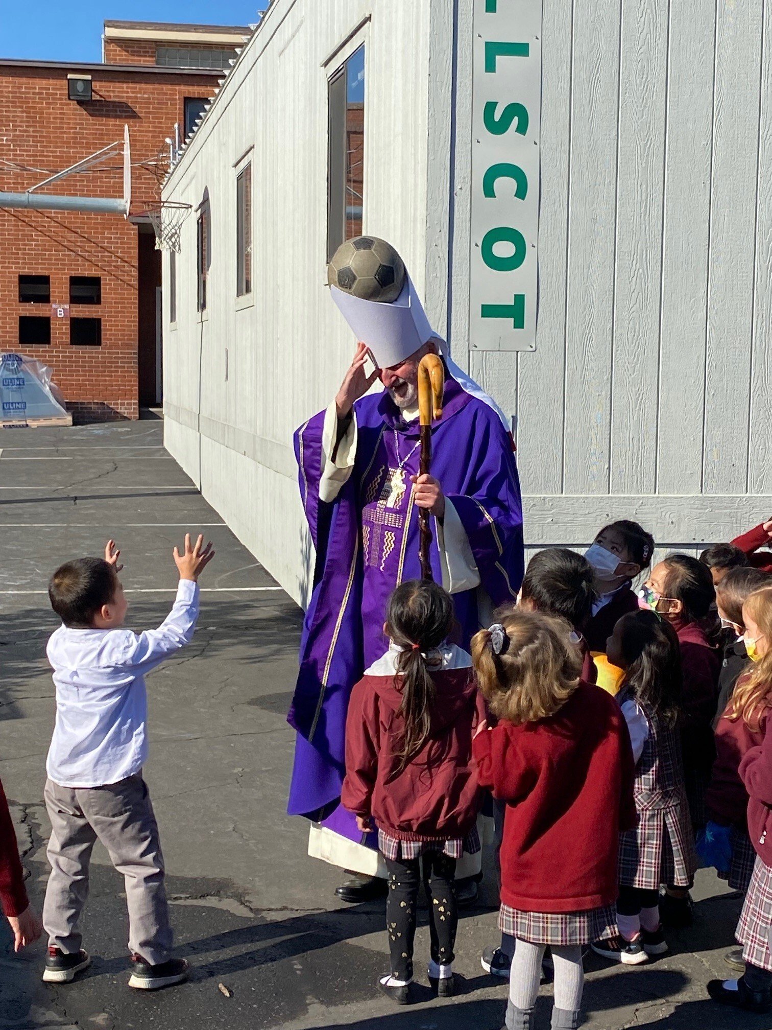 Bishop David O'Connell has a lighthearted moment with students at All Souls World Language Catholic School in Alhambra by placing a soccer ball in his miter. (Dr. Patrick Allison)