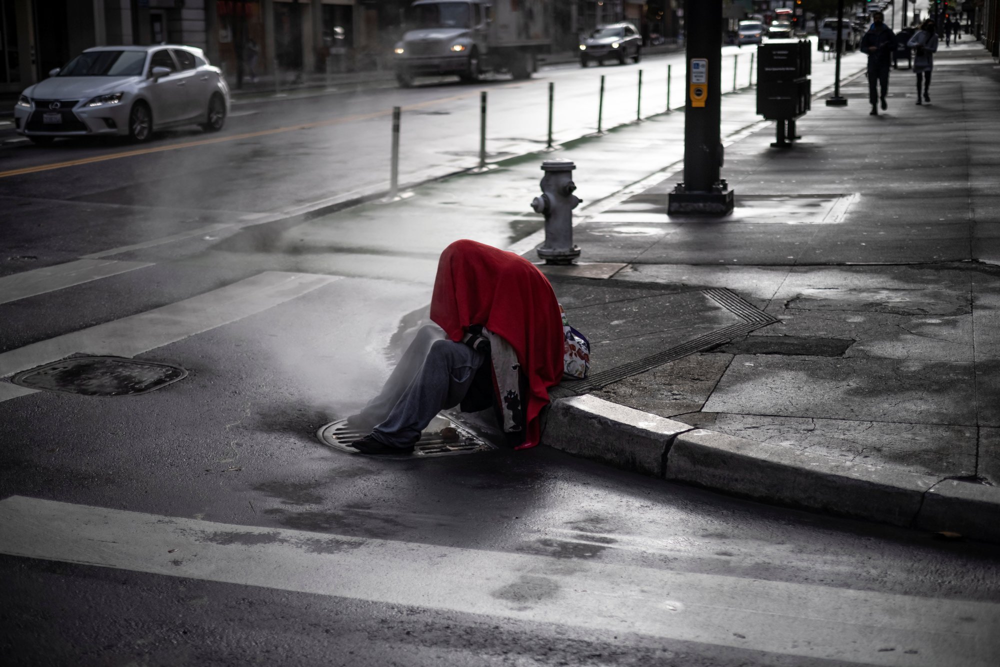 A homeless person in San Francisco sits on a corner as steam emerges from a vent Oct. 22, 2021. (CNS/Carlos Barria, Reuters)