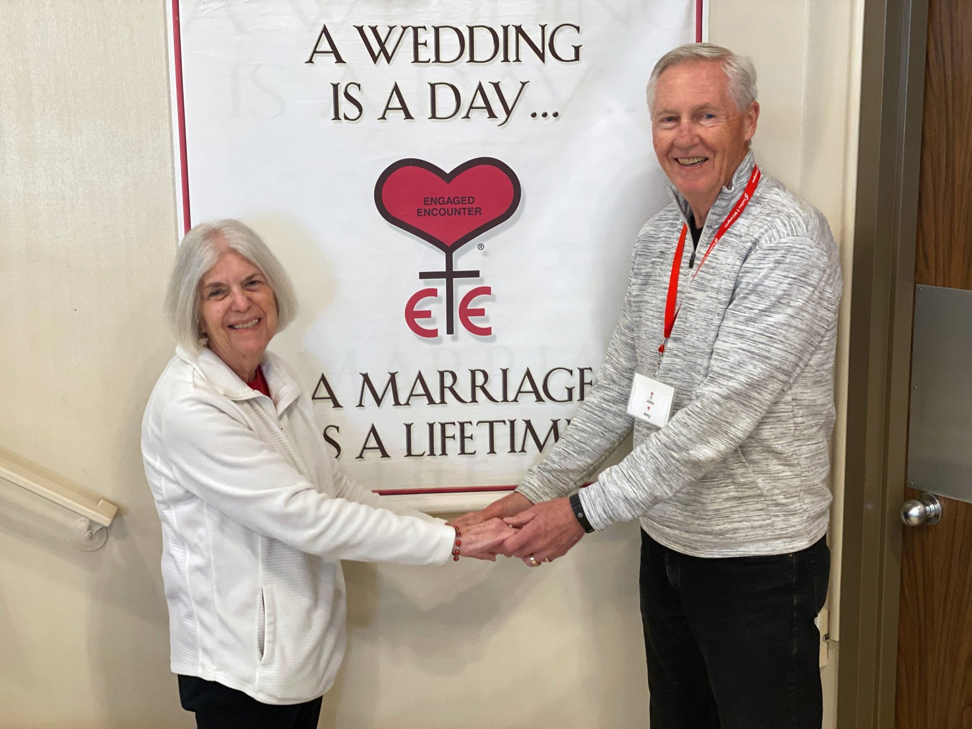 John and Amy Sabol, who volunteer with Catholic Engaged Encounters retreats, pose with their wedding photo near a poster listing the weekend’s themes. (Theresa Cisneros)
