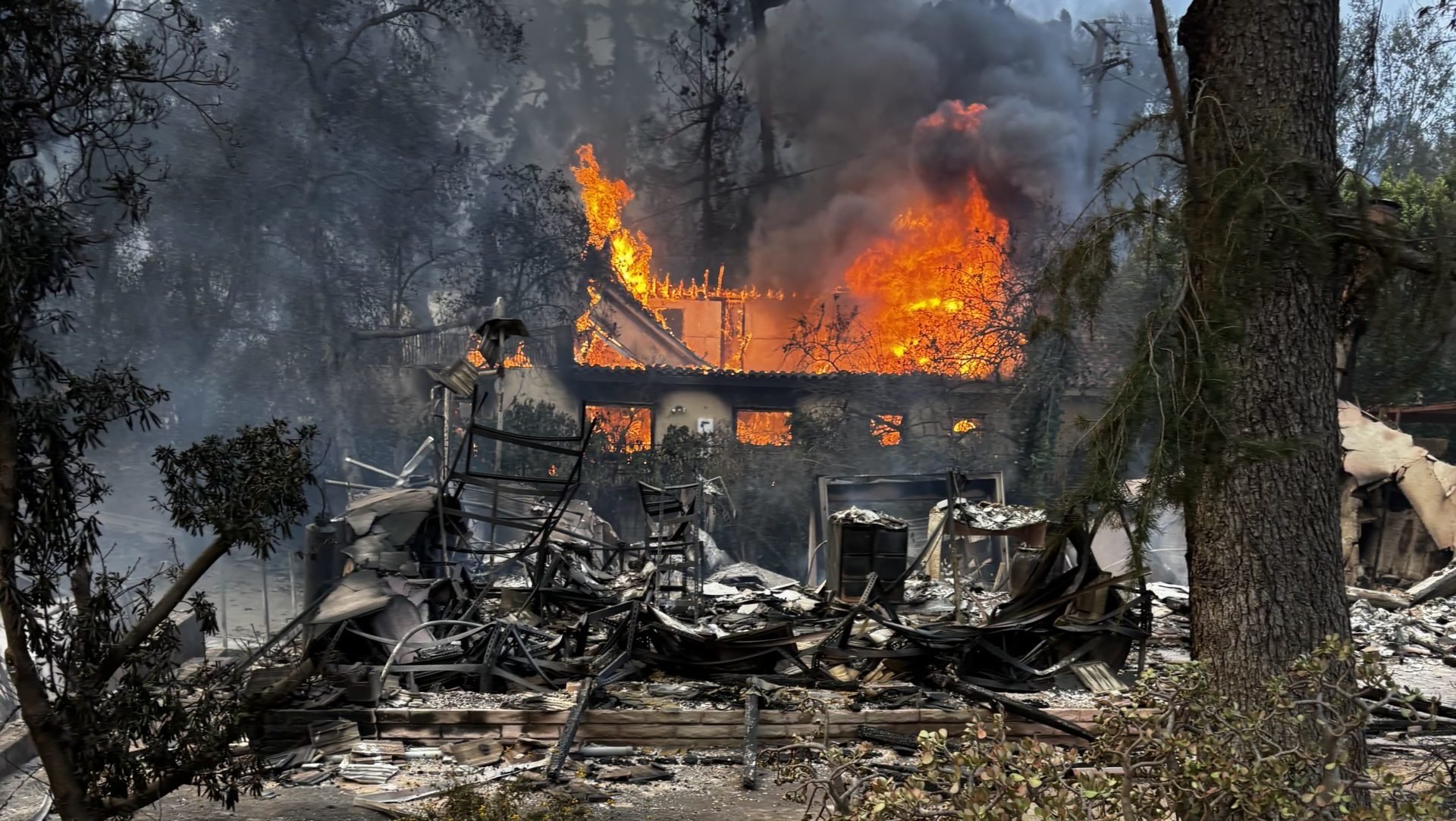 A home burns behind the wreckage of Trena Spurlock’s home during the Eaton Fire. (Trena Spurlock)