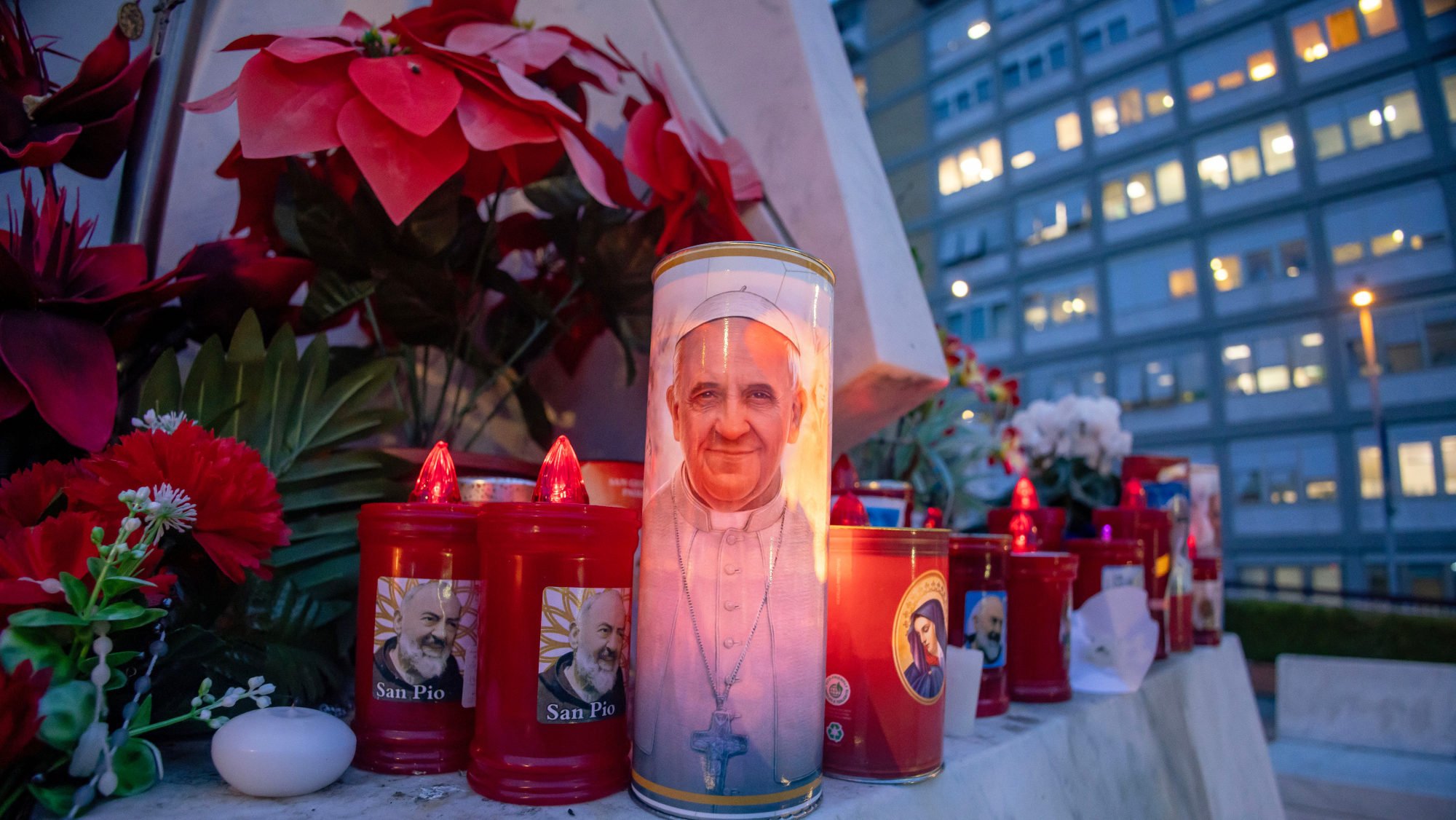 Votive candles and flowers are seen at the base of a statue of St. John Paul II outside Rome's Gemelli hospital Feb. 19, 2025, where Pope Francis is listed in "critical" condition. (CNS/Pablo Esparza)