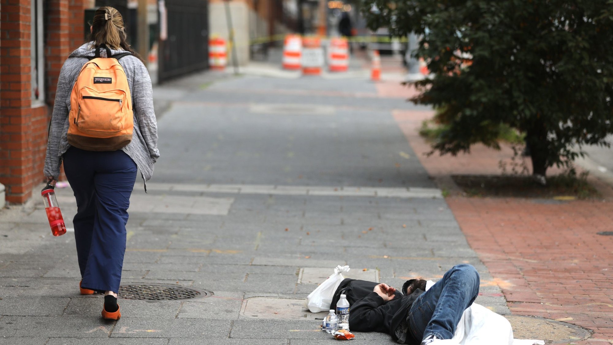A woman walks past a homeless man sleeping on a sidewalk in Baltimore June 6, 2023. (OSV News/Bob Roller)