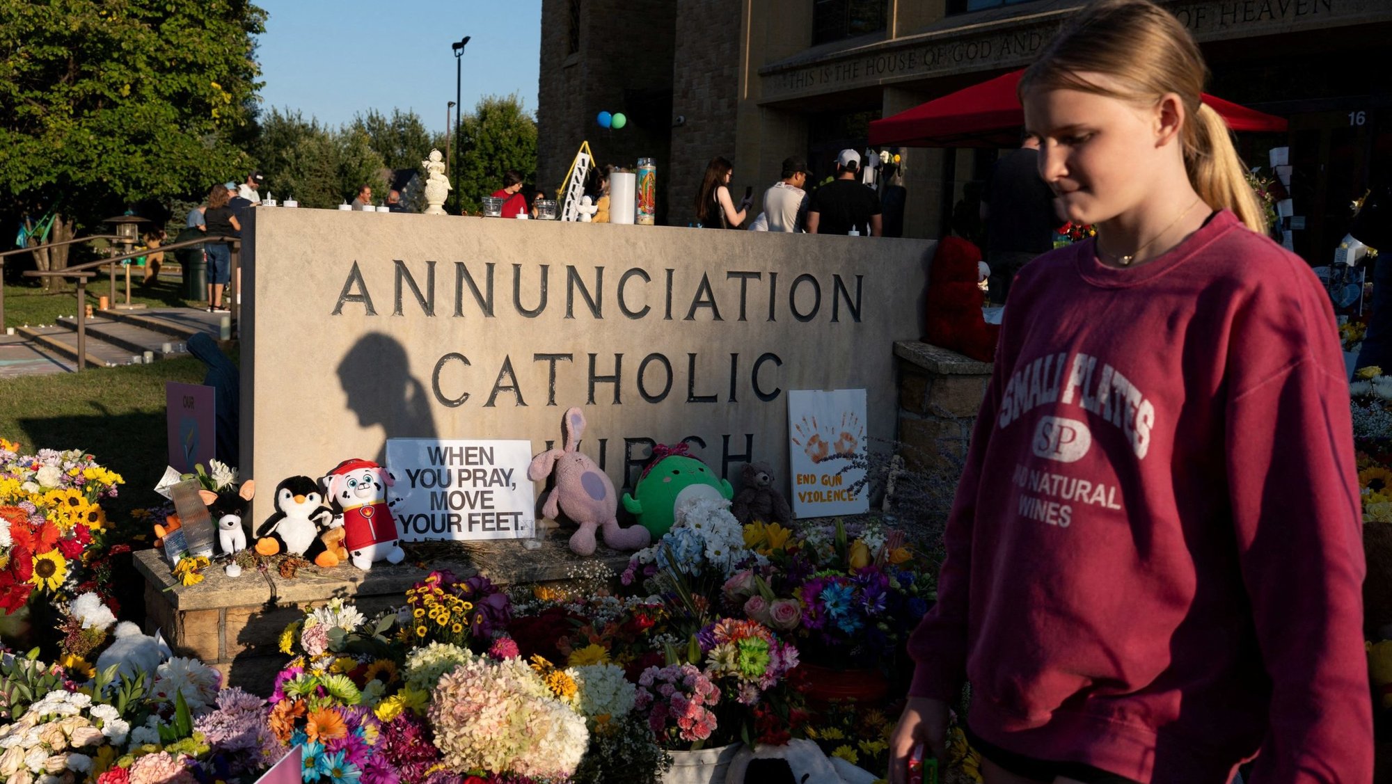 A young woman walks past a memorial outside Annunciation Church in Minneapolis Aug. 30, 2025, which is a home to an elementary school and was the scene of a shooting. The shooter opened fire with a rifle through the windows of the school's church and struck children attending Mass Aug. 27 during the first week of school, killing two and wounding 18 others. (OSV News photo/Tim Evans, Reuters)