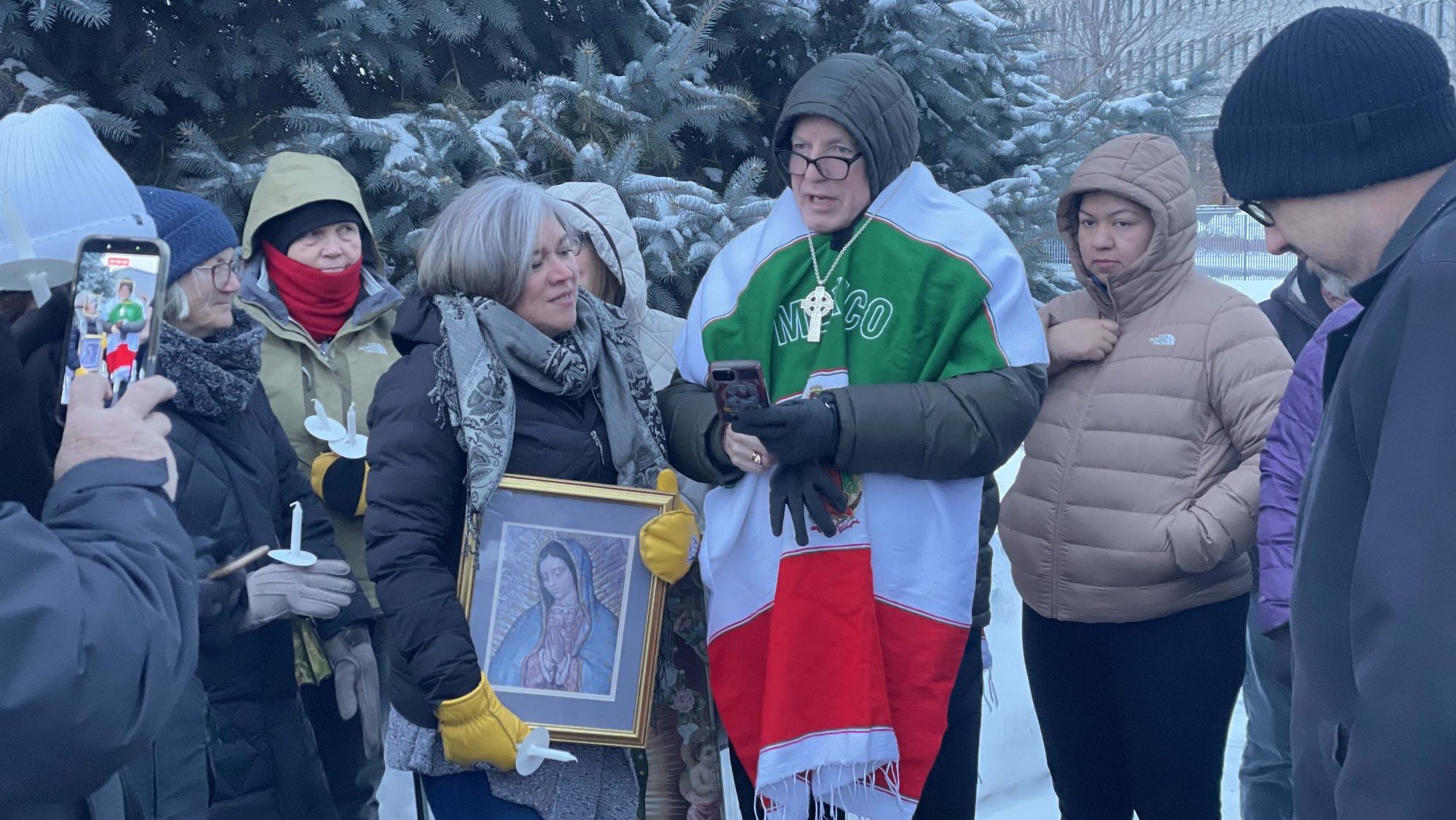 Auxiliary Bishop Kevin T. Kenney of St. Paul and Minneapolis, wearing a poncho with the colors of the Mexican flag, sings "Sancta Maria" during an impromptu prayer service Dec. 12, 2025, outside the B.H. Whipple Federal Building at Fort Snelling in the Twin Cities after a member of the local Catholic community was detained by officers with Immigration and Customers Enforcement. (OSV News photo/Josh McGovern, The Catholic Spirit)