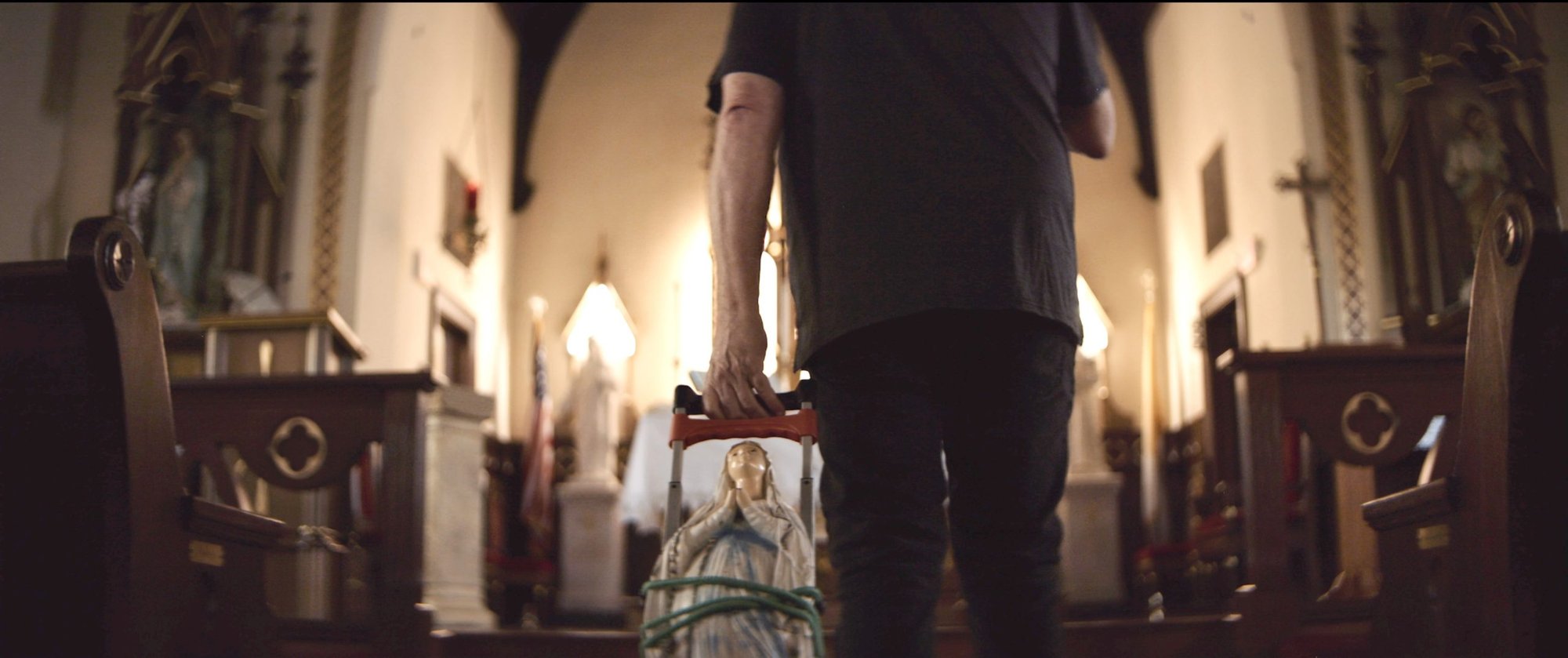 Kevin Matthews is pictured wheeling the statue of “Our Lady of the Broken” down the center aisle of St. James at Sag Bridge Catholic Church in Lemont, Illinois, in a scene from the film “Broken Mary.” (OSV News/Courtesy of ODB Films)