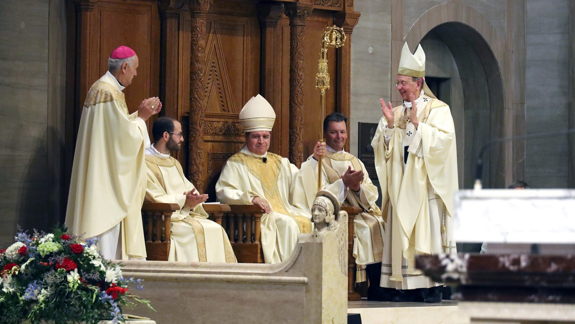 Bishop Evelio Menjivar-Ayala is seated in the cathedra, or bishop's chair, during his installation as the 10th bishop of Wheeling-Charleston, W.Va., July 2, 2026, at the Cathedral of St. Joseph in Wheeling. Archbishop Gabriele G. Caccia, apostolic nuncio to the U.S., left, Archbishop William E. Lori of Baltimore, right, and clergy look on, applauding. (OSV News photo/Colleen Rowan, The Catholic Spirit)