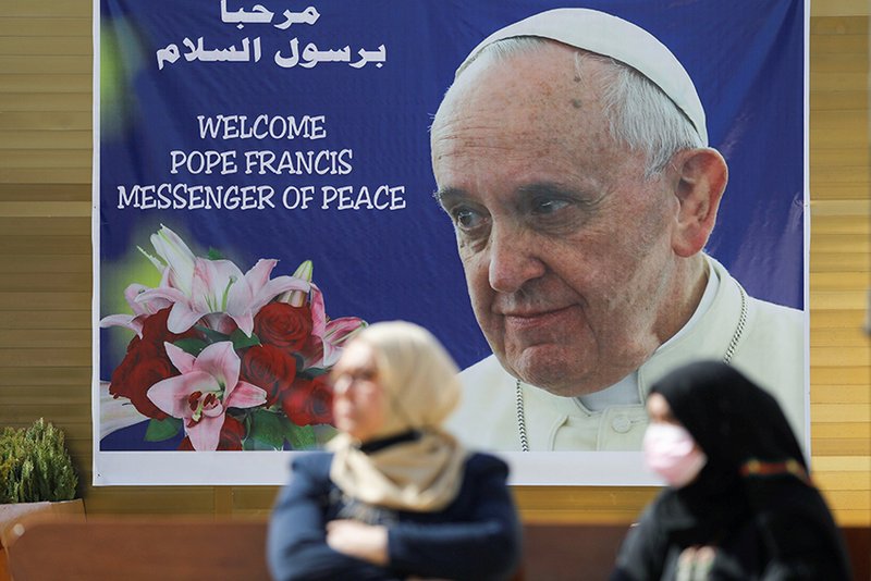 Mujeres se paran cerca de un cartel del Papa Francisco en Bagdad el 3 de marzo. El Papa Francisco tiene previsto visitar Irak del 5 al 8 de marzo. (Foto CNS/Khalid al-Mousily, Reuters)