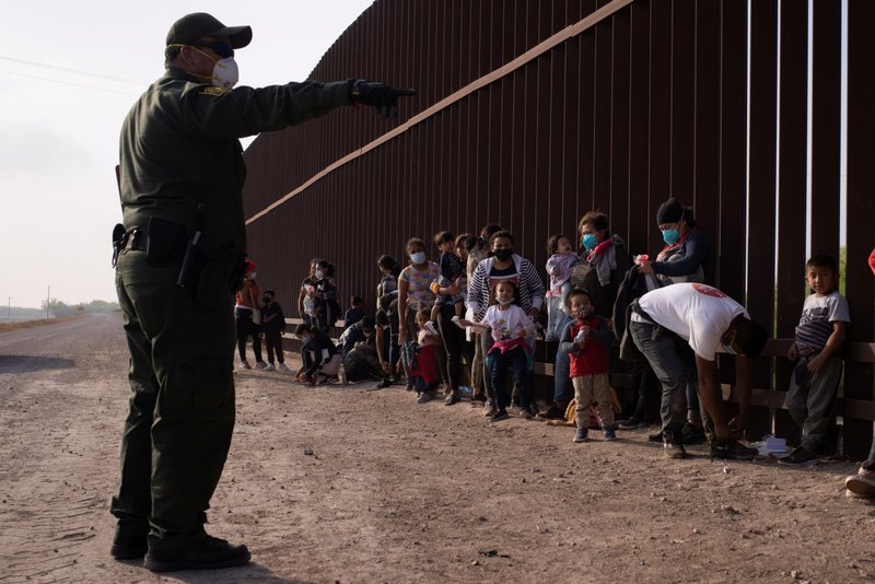 Un agente de la Patrulla Fronteriza en Peñitas, Texas, instruye a los migrantes que buscan asilo el 17 de marzo de 2021, mientras hacen fila a lo largo del muro fronterizo después de cruzar el Río Bravo. El Servicio de Control de Inmigración y Aduanas dice que la agencia ha documentado más de 12,000 casos de coronavirus en centros de detención hasta la fecha. (Foto CNS/Adrees Latif, Reuters)