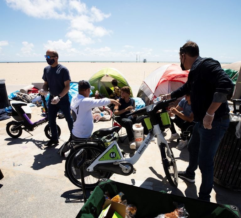 Mike Psomas (derecha) y Chris Seminatore (izquierda) de la Orden de Malta resuenden comida y agua a los residentes sin hogar del paseo marítimo de Venice Beach. (Víctor Alemán)