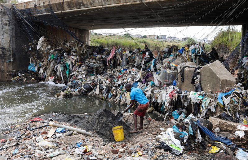 Un hombre recoge arena frente al plástico reciclable atrapado que fue arrastrado bajo el puente en Olifantsfontein, Sudáfrica, 29 de marzo de 2021. El Día de la Tierra, que se celebra el 22 de abril de cada año, marca el aniversario del nacimiento del movimiento ambiental moderno en 1970. (Foto CNS/Siphiwe Sibeko, Reuters)