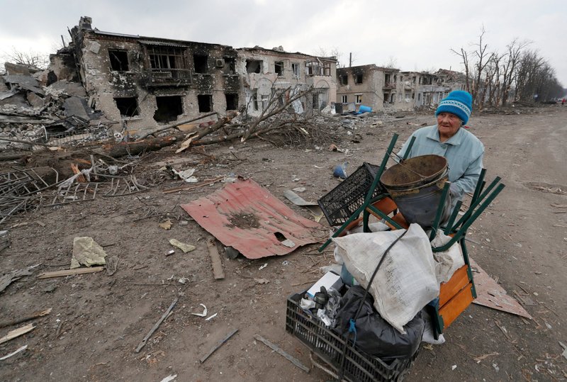 Una mujer empuja un carrito con sus pertenencias el 15 de marzo de 2022, frente a edificios dañados durante ataques de Rusia en la ciudad de Volnovakha, Ucrania, controlada por separatistas. (Foto CNS/Alexander Ermochenko, Reuters)