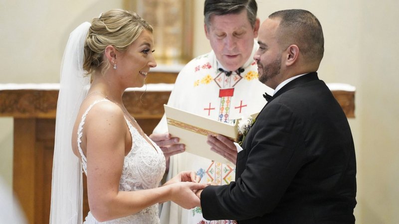Christina MacDougall coloca una alianza en el dedo de Julio Prendergast mientras Monseñor Francis J. Schneider oficia su misa de bodas el 20 de agosto de 2021, en la Iglesia de San Juan Bautista en Wading River, N.Y. (Foto CNS /Gregory A. Shemitz)