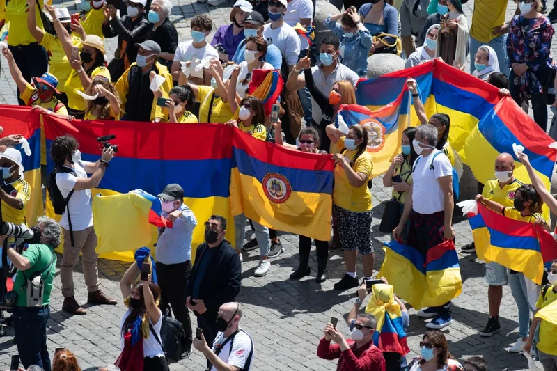 Personas sostienen la bandera nacional de Colombia mientras el Papa Francisco dirige el "Regina Coeli" desde la ventana de su estudio con vista a la Plaza de San Pedro en el Vaticano el 9 de mayo de 2021. El papa hizo un llamamiento a la paz en Jerusalén, Afganistán y Colombia. (Foto CNS/Vatican Media).