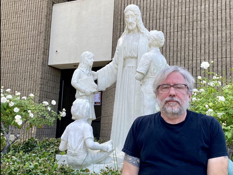 Michael Stucchi posa delante de la estatua restaurada de Jesús con niños en la iglesia de San Mel en Woodland Hills. (Tom Hoffarth)