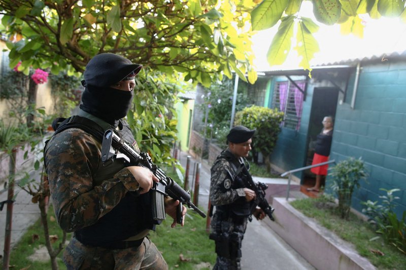 Una señora se para en una puerta mientras tropas armadas salvadoreñas patrullan un área residencial en Soyapango el 5 de diciembre de 2022. Una represión masiva contra las pandillas en El Salvador ha llevado a continuos abusos contra los derechos humanos, dice un nuevo informe. (Foto CNS/José Cabezas, Reuters)