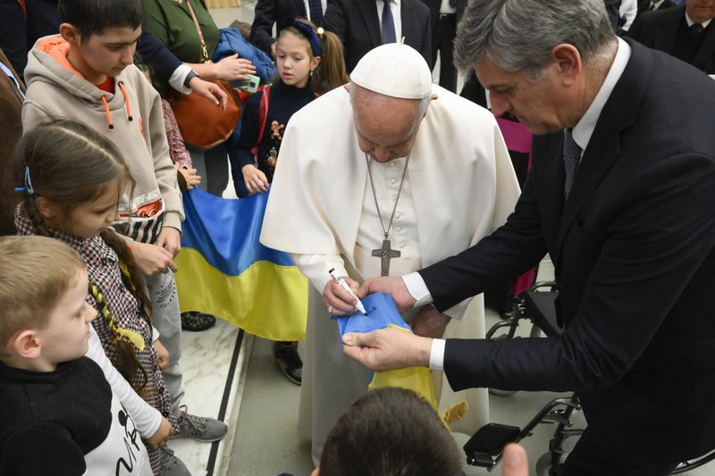 El Papa Francisco firma una bandera ucraniana para un niño ucraniano al final de su audiencia general semanal del 22 de febrero de 2023, en la sala de audiencias del Vaticano. Durante la audiencia, el Papa señaló que el aniversario de la invasión rusa de Ucrania es el 24 de febrero y rezó por el fin de la guerra. (CNS/Vatican Media