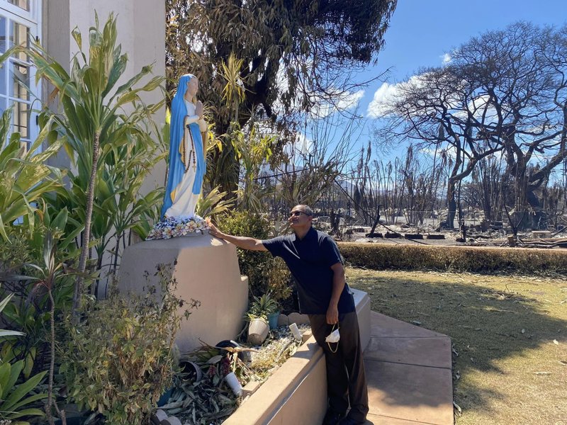 Misioneros de la Fe El padre Kuriakose Nadooparambil, párroco de la iglesia Maria Lanakila de Lahaina (Maui), toca una estatua de la Virgen María que aún permanece en pie entre el follaje intacto por el incendio forestal que calcinó los árboles al otro lado de la calle y destruyó toda la ciudad de Lahaina. (Maria Lanikila Parish)
