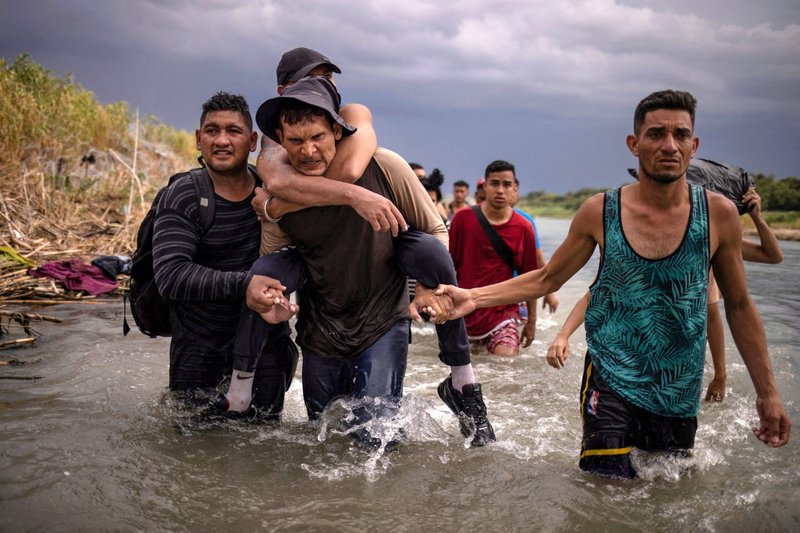 Los compatriotas Douglas y David ayudan a León, un migrante de Venezuela, mientras carga a su primo discapacitado Luis el 15 de septiembre de 2023, después de cruzar el Río Grande desde México a Estados Unidos. Los migrantes buscaban un punto de entrada pasando el alambre de púas en Eagle Pass, Texas. (Foto de OSV News/Adrees Latif, Reuters)