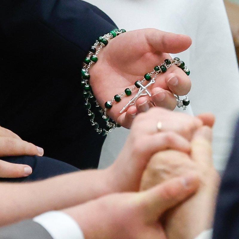 Una persona sostiene un rosario mientras el Papa Francisco saluda a parejas de recién casados al final de su audiencia general semanal en el Aula de Audiencias Pablo VI en el Vaticano el 23 de agosto de 2023. (Foto CNS/Lola Gomez)