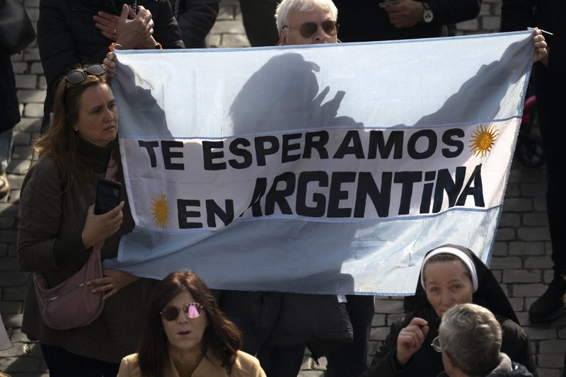 Una pareja en la Plaza de San Pedro del Vaticano sostiene un cartel sobre una bandera argentina que dice: "Te esperamos en Argentina", mientras el Papa Francisco dirige el rezo de la oración del Ángelus el 14 de enero de 2024. (Foto de CNS/Vatican Media)