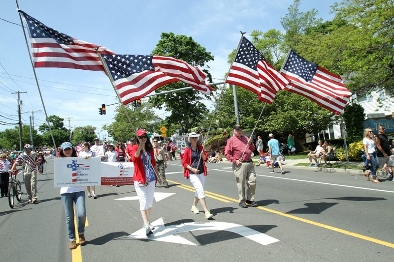 Miembros de Católicos por la Libertad Religiosa portan banderas estadounidenses mientras marchan en un desfile del Día de los Caídos en Setauket, Nueva York, el 26 de mayo de 2014. El primer informe anual "Estado de la libertad religiosa en los Estados Unidos" de la Conferencia de Obispos Católicos de los Estados Unidos, publicado el 16 de enero de 2024, identifica cinco amenazas principales a la libertad religiosa en los Estados Unidos, incluyendo una regulación federal que dice podría imponer mandatos a los médicos para realizar procedimientos objetables y amenazas al servicio de la iglesia a las personas que son migrantes. (OSV News /Gregory A. Shemitz)