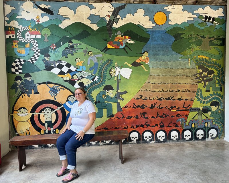 La hermana de la Providencia Vilma Franco se sienta en un banco en su ciudad natal de Arcatao, El Salvador, el 27 de abril de 2024, frente a un mural que representa la masacre de 1980 en el río Sumpul. Cada año, organizaciones como la Asociación Sumpul recuerdan la masacre de más de 600 personas por las fuerzas armadas salvadoreñas, un esfuerzo para educar y prevenir que tales actos se repitan. (Foto OSV News/Rhina Guidos, GSR)