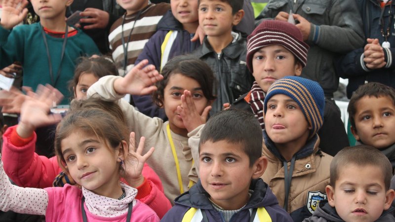 Una foto de archivo de 2015 muestra a niños yezidíes iraquíes desplazados saludando a trabajadores del Catholic Relief Service y a una delegación de la Conferencia de Obispos Católicos de Estados Unidos, encabezada por el obispo Oscar Cantu, durante una visita al Colectivo Sharia, Irak. (Foto OSV News/Dale Gavlak)