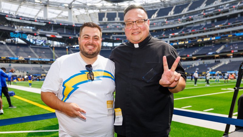 El padre Richard Sunwoo, a la derecha, posa con Niko Rudela, hermano del padre Marko Rudela, durante un partido de pretemporada de los Chargers el 17 de agosto. (Los Angeles Chargers)