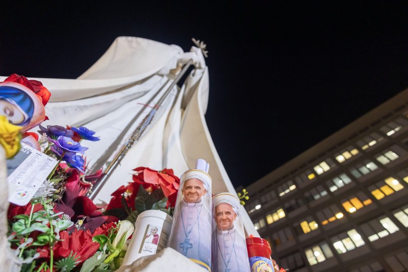 Velas votivas y flores se ven en la base de una estatua de San Juan Pablo II fuera del hospital Gemelli de Roma el 21 de febrero de 2025, donde el Papa Francisco está siendo tratado por una neumonía doble. (CNS photo/Pablo Esparza)